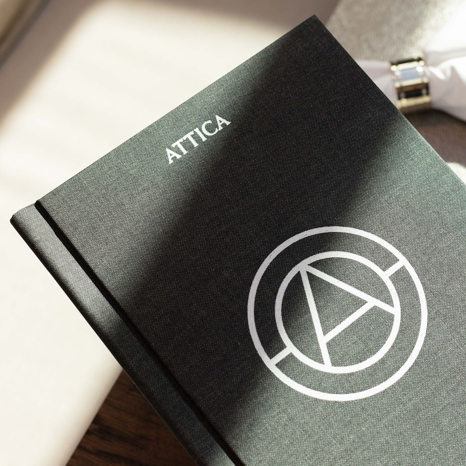 Grauer ATTICA-Bucheinband mit deutlich sichtbarem Logo und Symbol in allen Einzelheiten.