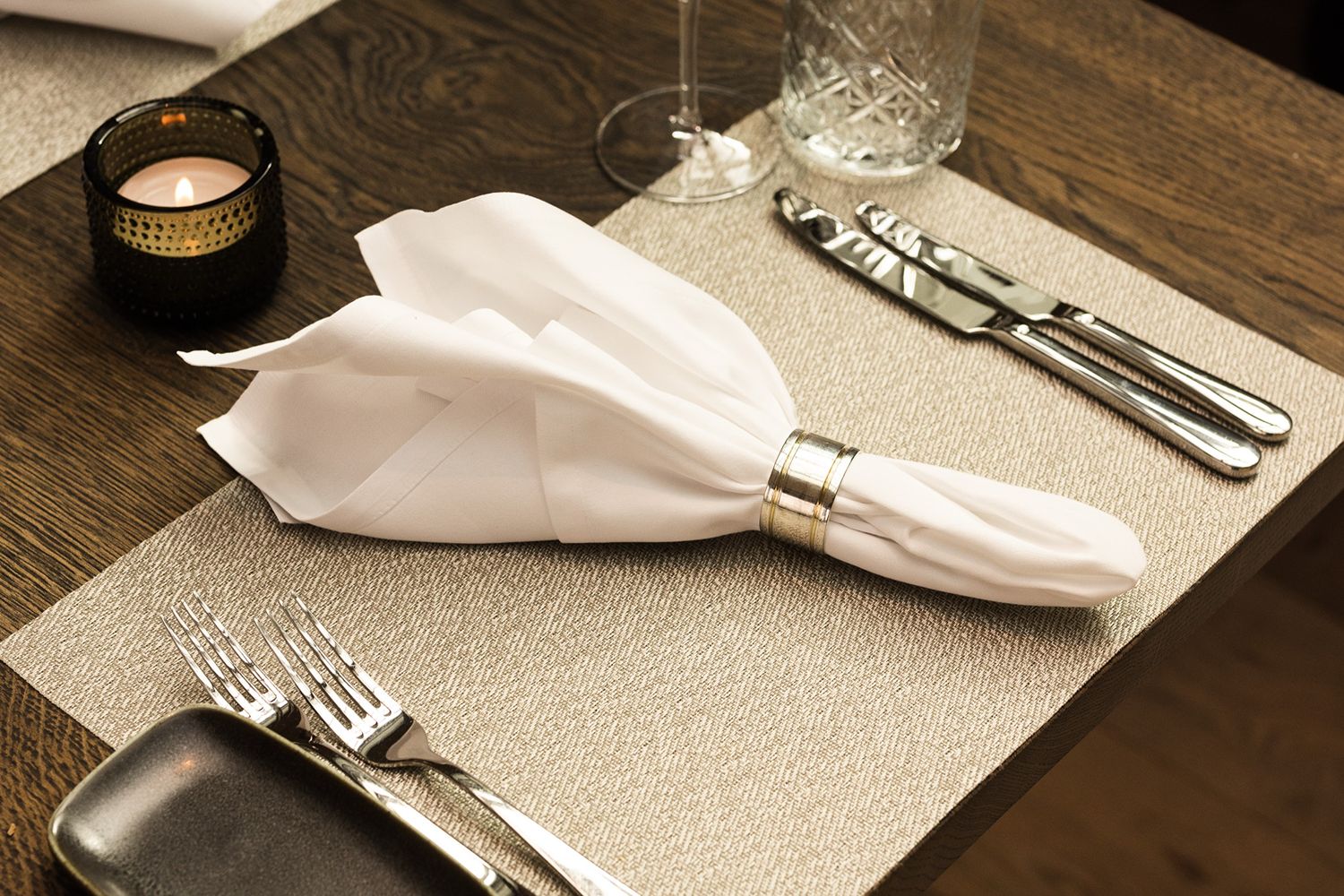 Elegantes Esstischgedeck mit feinem Silberbesteck und Kristallgläsern auf einem Tischset.