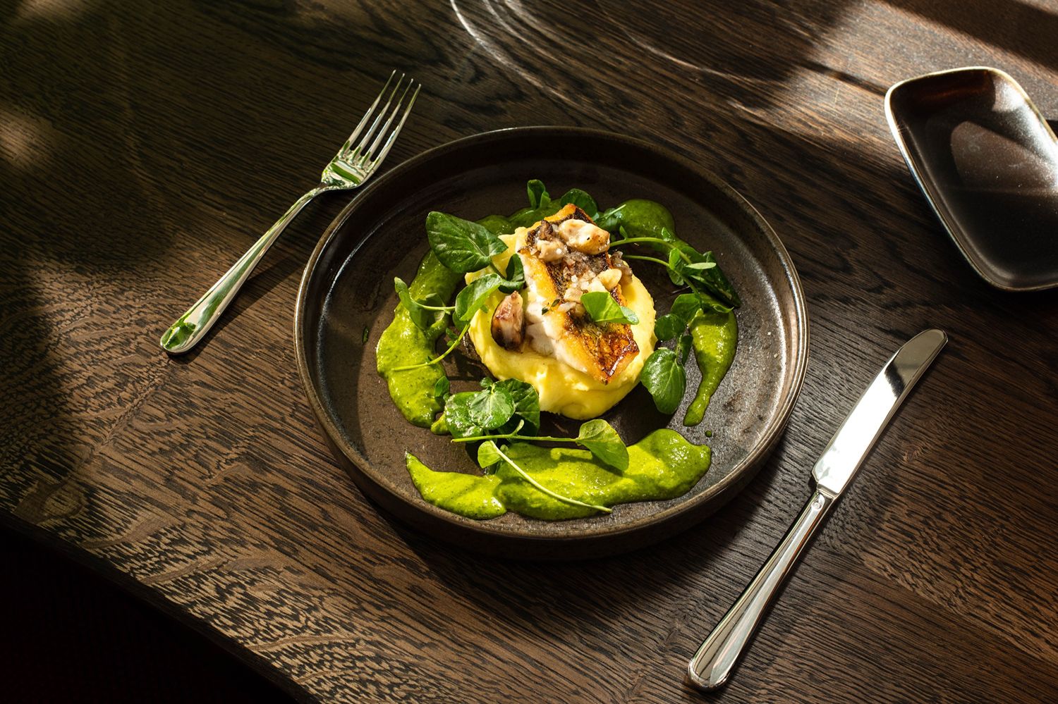 Gegrillte Meeresfrüchte mit cremigem Kartoffelpüree und einer leuchtend grünen Sauce auf einem warmen Teller.