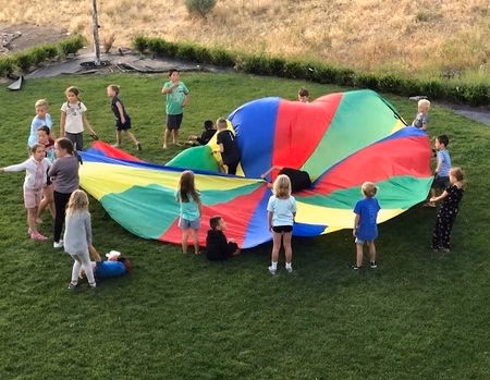 Group of children on grass playing with a colorful parachute outdoors.