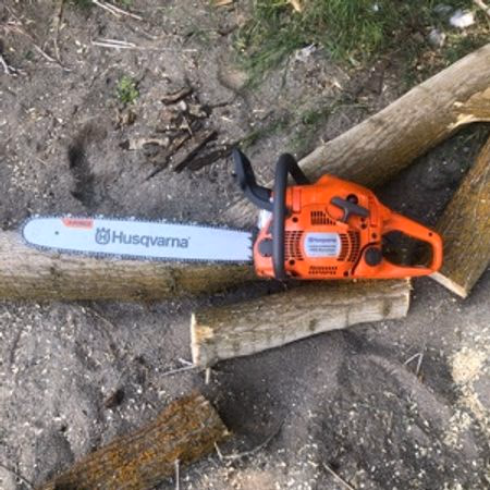 Orange Husqvarna chainsaw lying on cut logs on dirt ground with some grass.