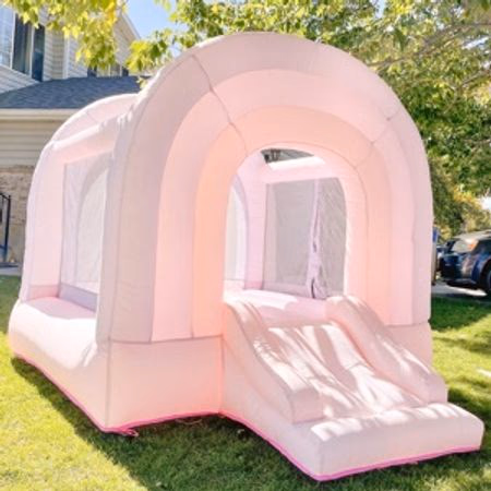Pink inflatable bounce house with slide set up on green grass in a sunny backyard.