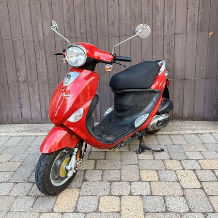 Red motor scooter parked on a paved stone surface with a wooden wall background.