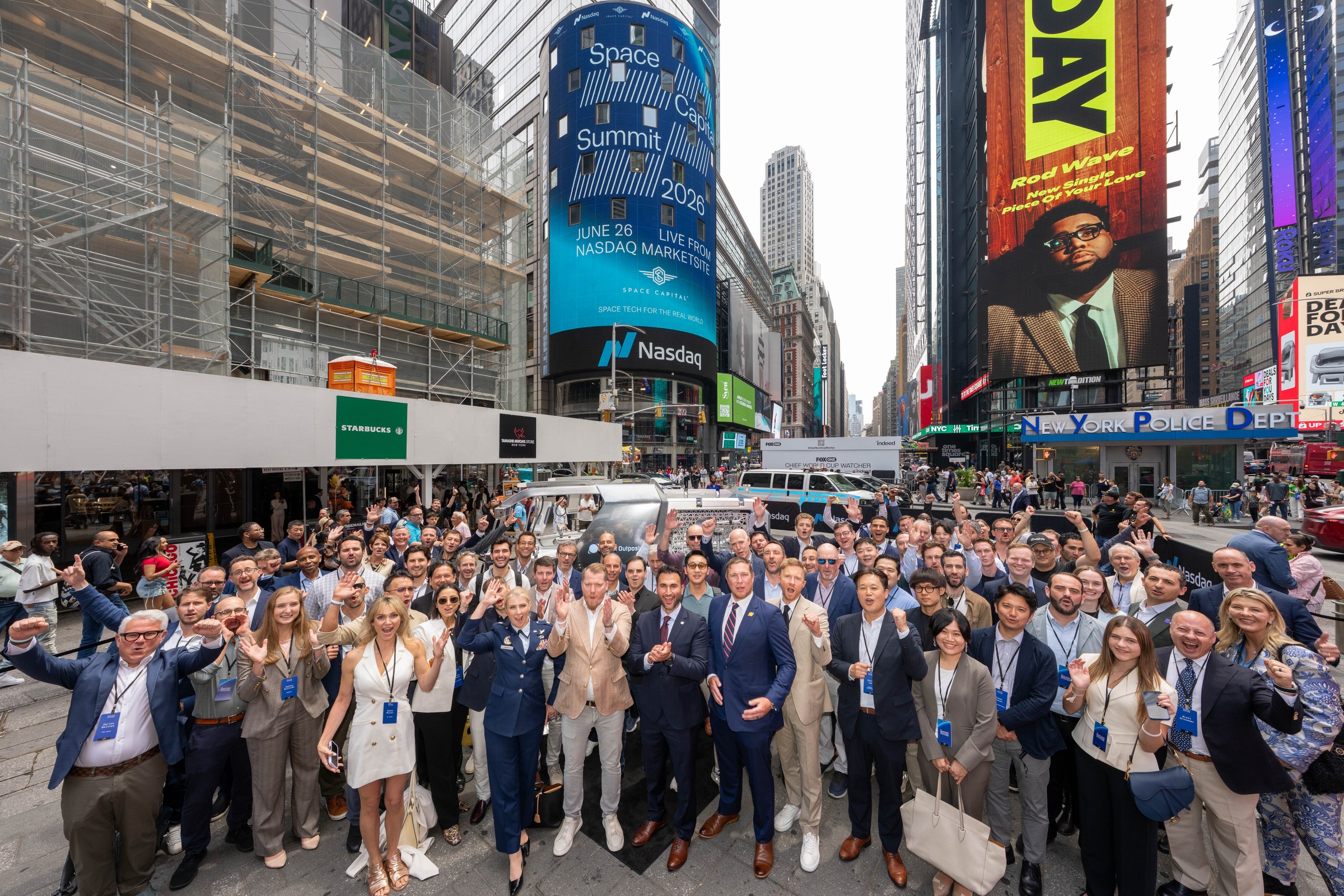 Large group of Space Capital Summit 2026 attendees gathered in Times Square, cheering and waving beneath the Nasdaq tower displaying the Summit branding.