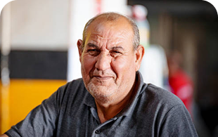Older man with serious expression wearing dark shirt in industrial setting