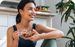 Woman smiling while holding bowl of healthy breakfast cereal in modern kitchen with plants