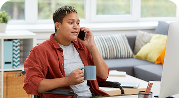 Man in red shirt talking on phone while holding coffee cup indoors.