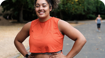 Smiling woman wearing orange sleeveless shirt standing outdoors with hands on hips