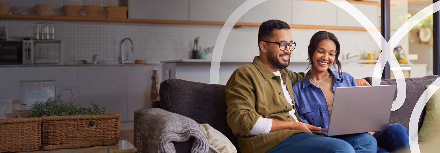 Couple smiling while using laptop together on couch in modern kitchen