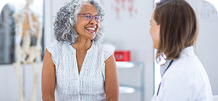 Two women conversing in a modern office setting with white walls and shelving
