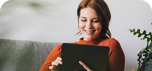 Woman in orange shirt sitting on couch, smiling while using digital tablet