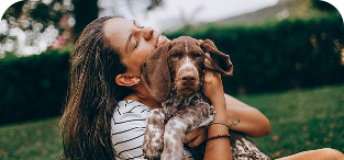 Woman smiling while holding brown dog outdoors in grass.