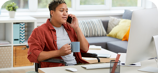 Man in red shirt talking on phone while working at computer desk