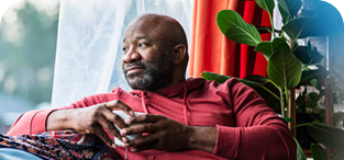 Man in red shirt sitting by window with potted plant