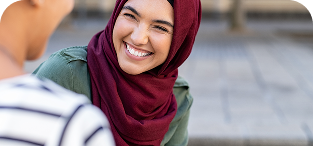 Smiling woman wearing burgundy hijab and olive jacket outdoors.