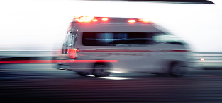 Red emergency ambulance with lights on driving at high speed on road