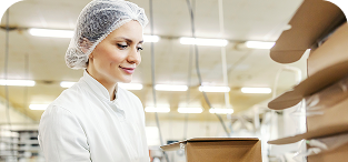 Woman in hair net and white coat working in commercial kitchen or bakery.
