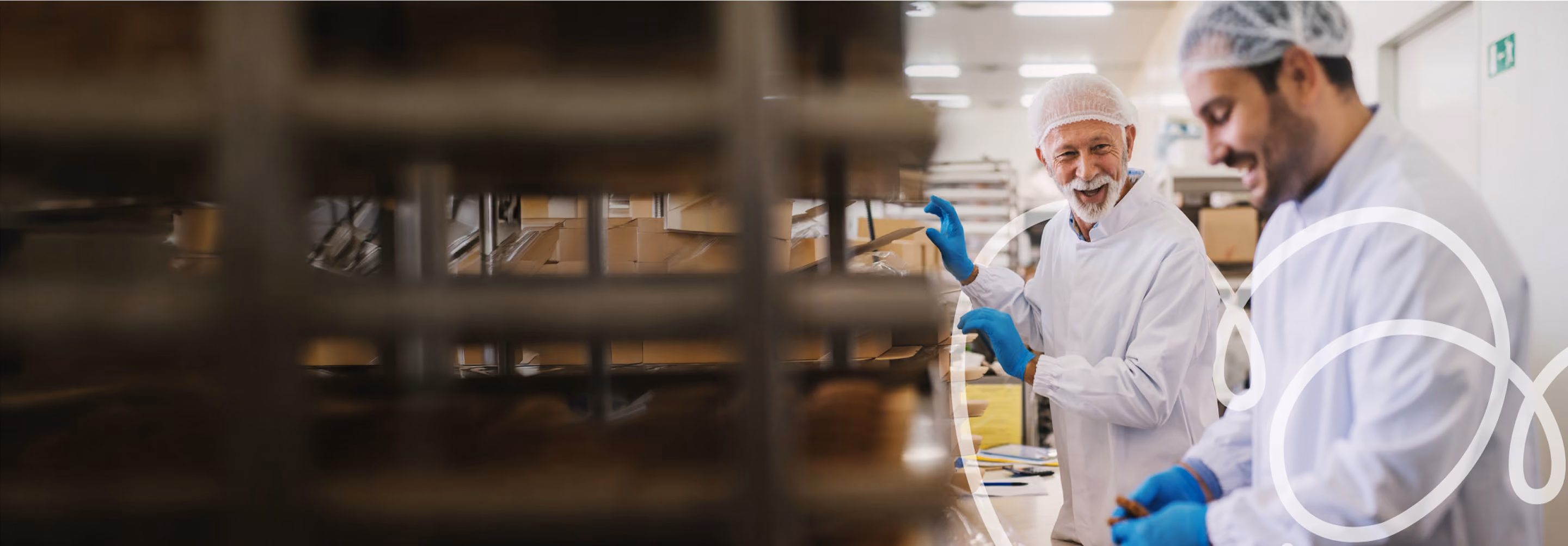 Two workers in white lab coats and hairnets discussing materials in an industrial facility