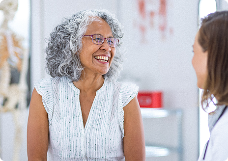 Smiling older woman with gray hair talking to a healthcare professional in a medical office.