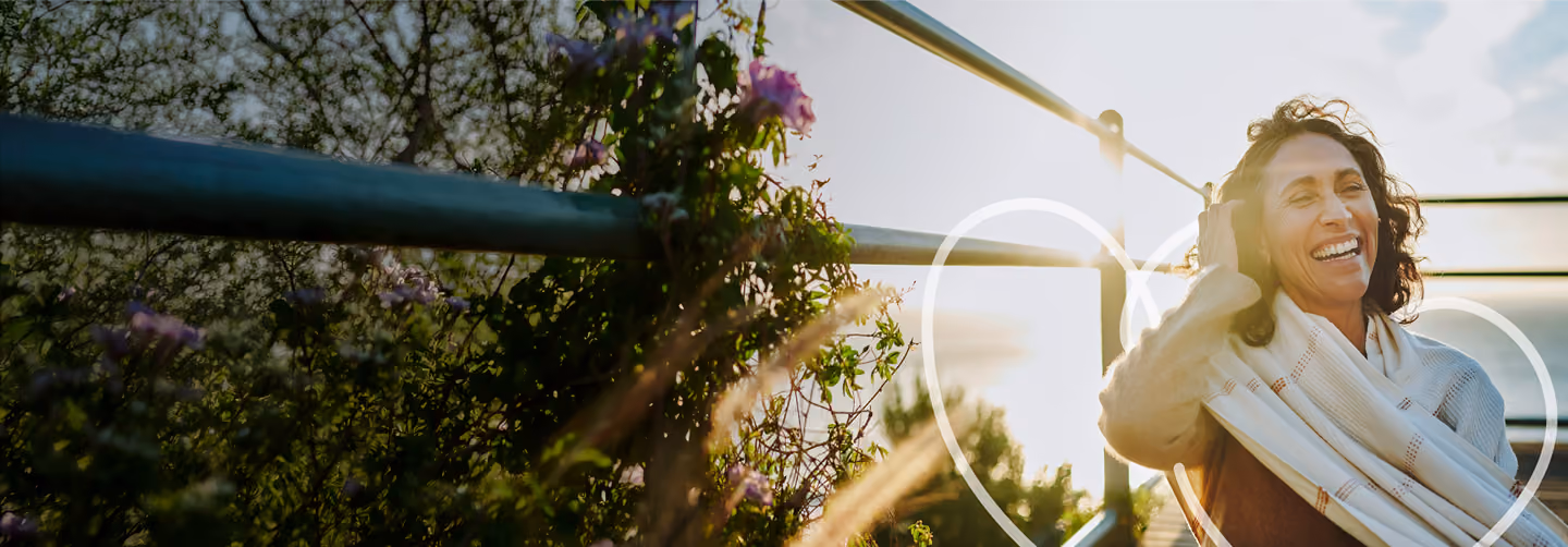 Smiling woman in white cardigan surrounded by purple flowers and climbing vines outdoors