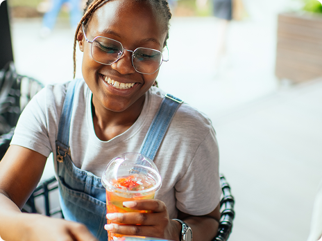 Smiling woman wearing glasses and denim apron holds glass of orange juice beverage