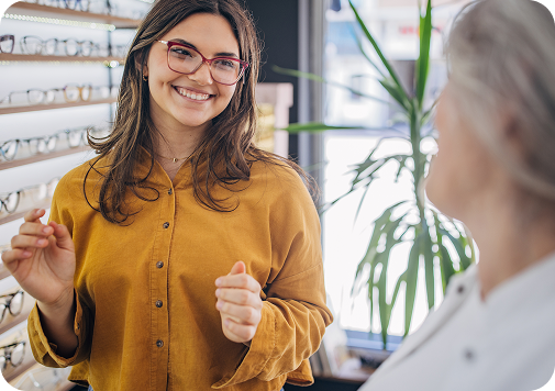 Smiling woman in yellow shirt wearing glasses speaks with customer in eyeglasses store