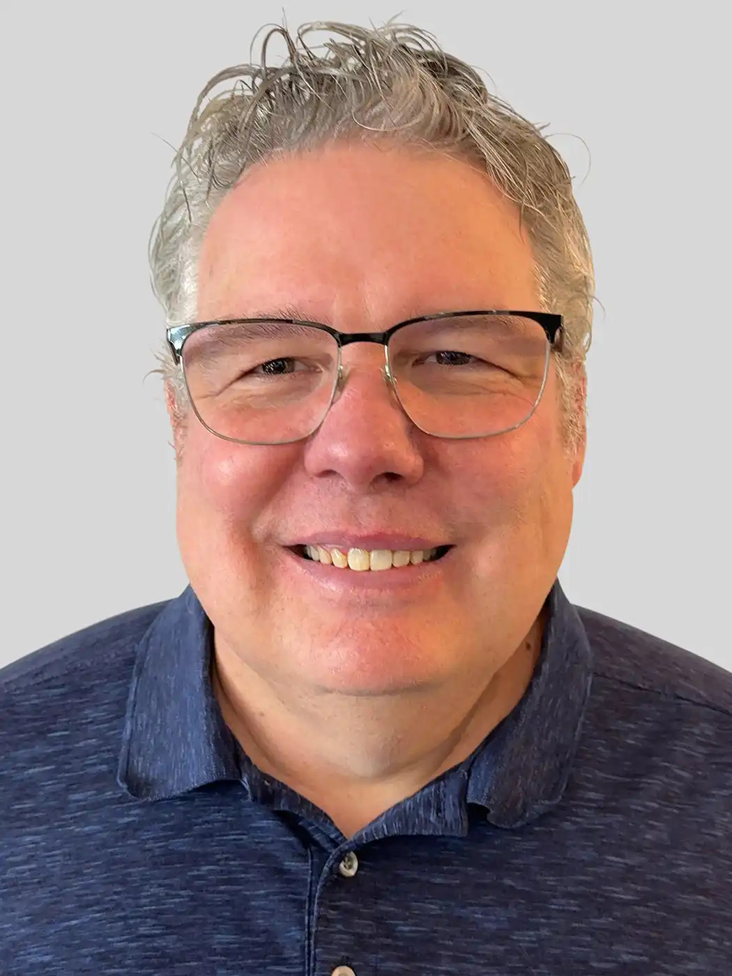 A headshot of a man smiling with silver hair wearing glasses