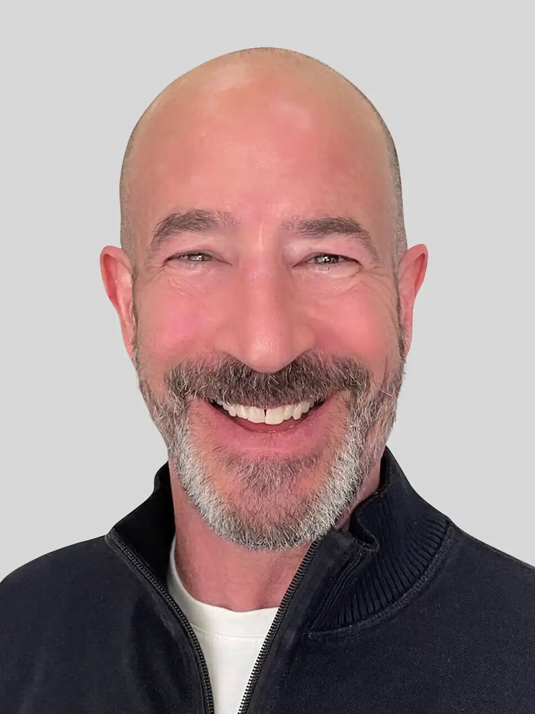 A headshot of a bald man smiling with a goatee wearing a dark blue sweater