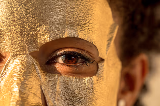 Close-up of a person’s eye framed by a shimmering gold facial mask
