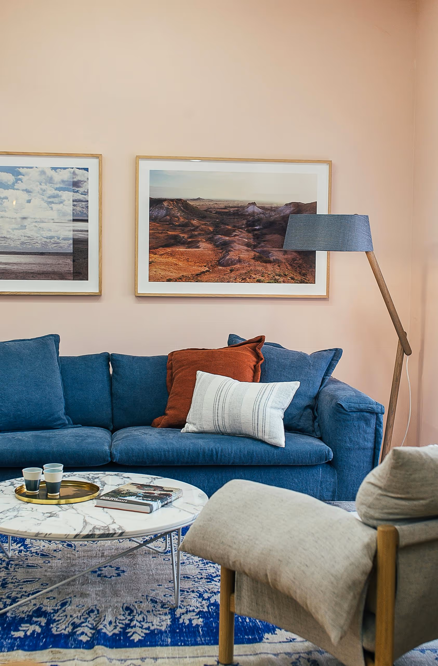 A living room featuring a coach, chair, coffee table, photo frames on the wall, and a lamp