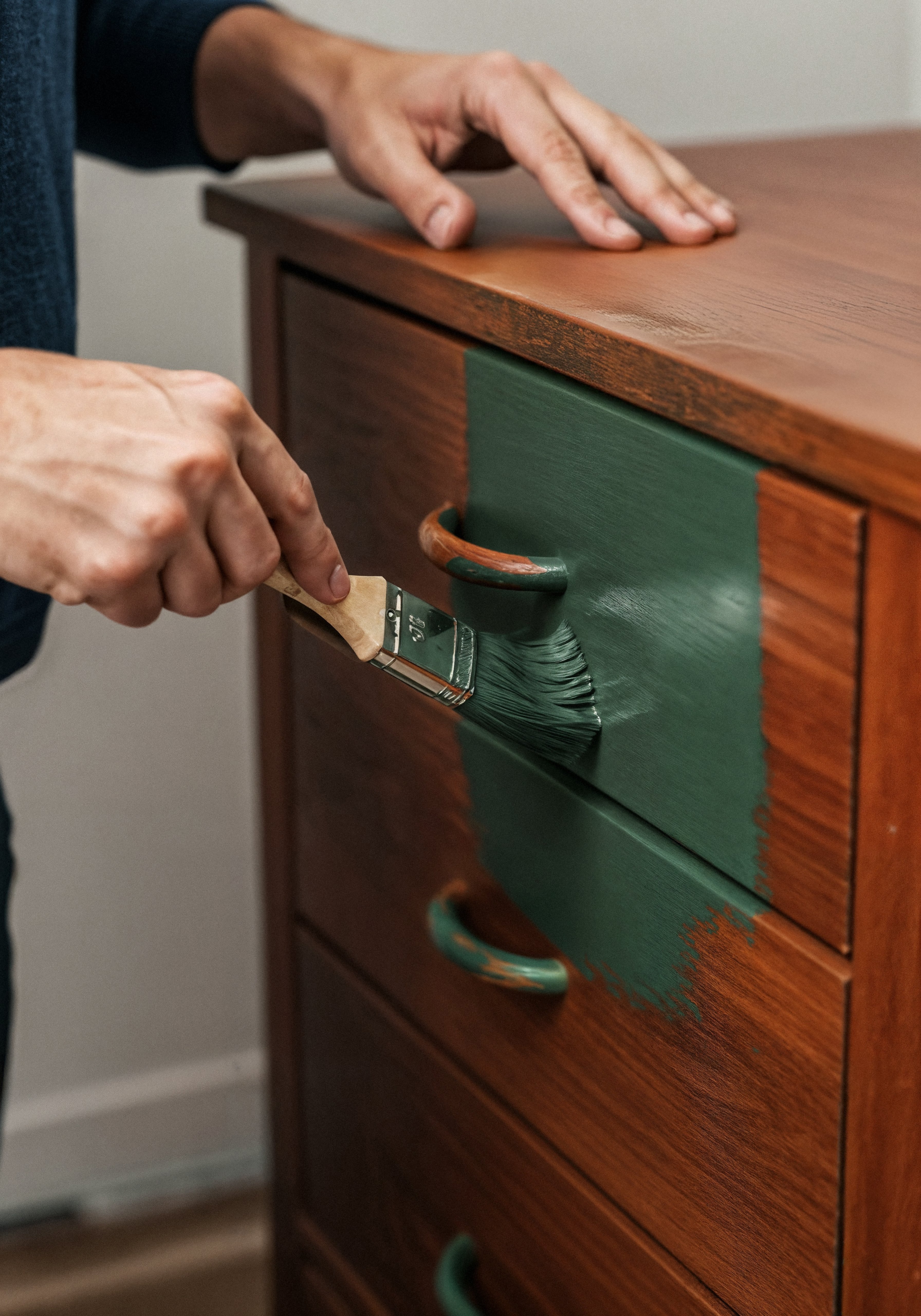 Painter painting a wooden cabinet green with a paint brush