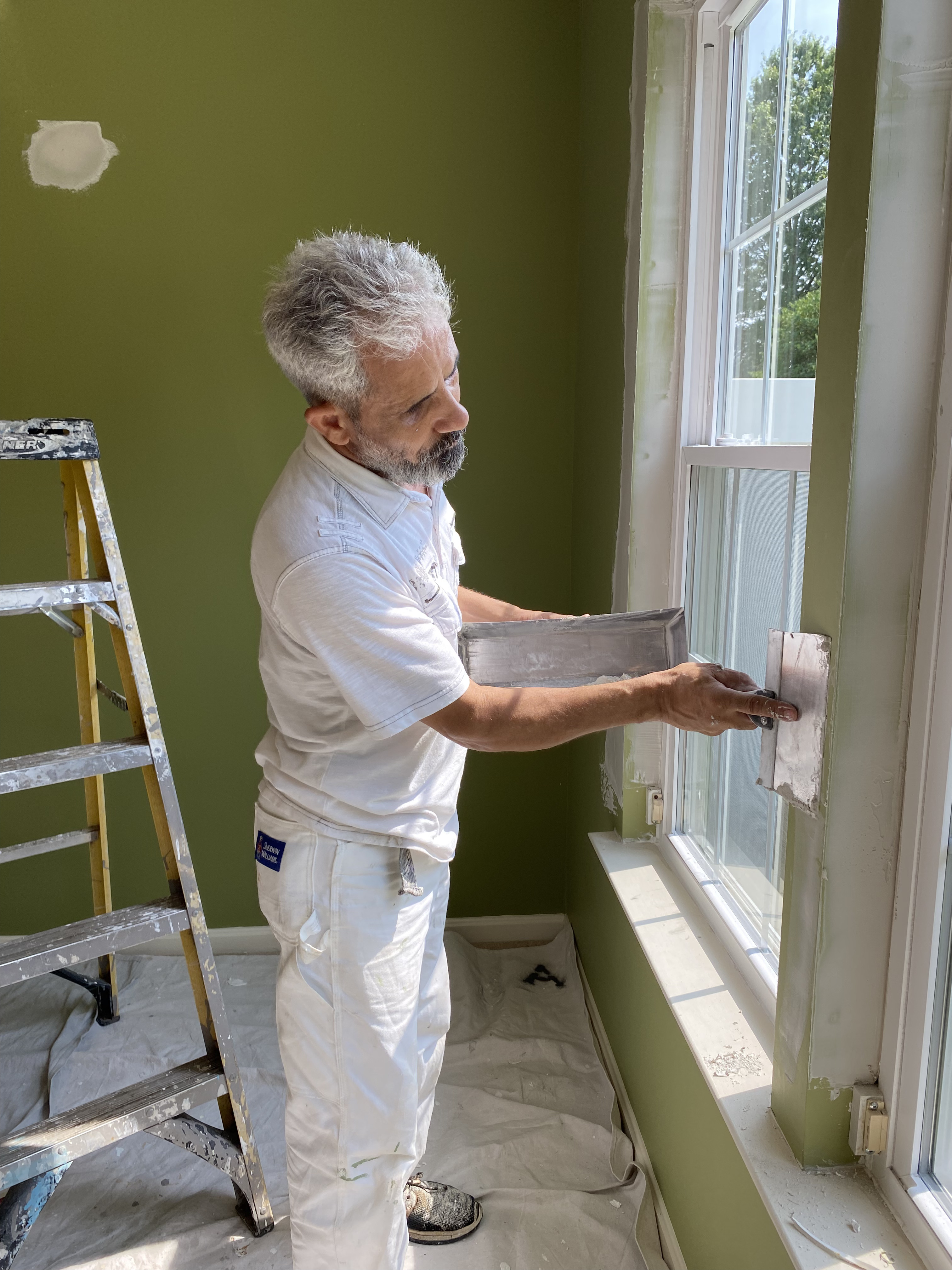 Ahmed from PrimePro Painting & Power Washing at work near the window area of a home with green walls