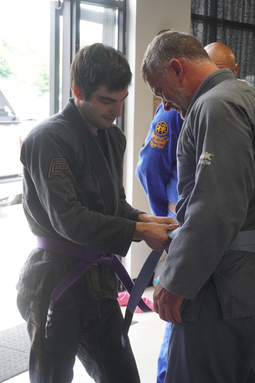 A man fastens a purple belt around another man at Horsemen Brazilian Jiu Jitsu in New Freedom, PA.