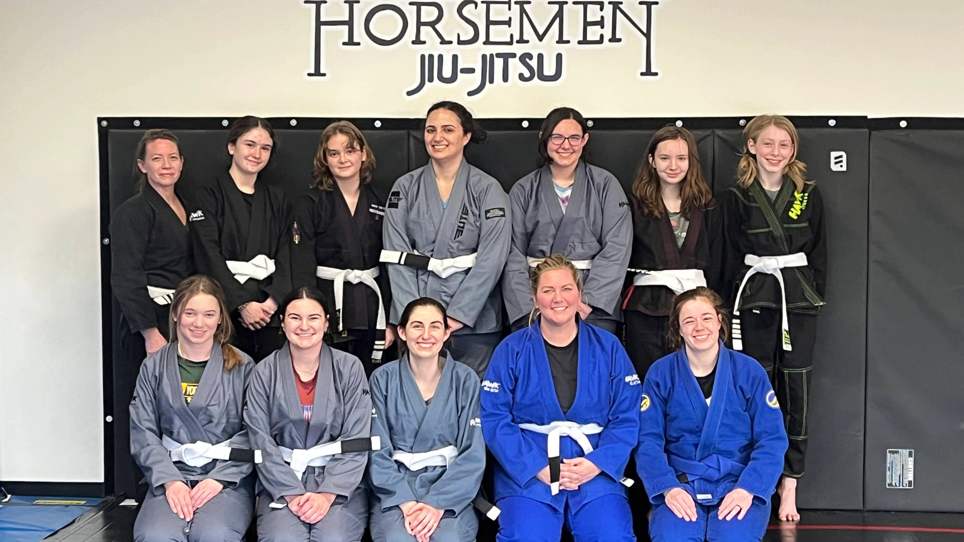A group of women smiling and posing together during a Brazilian Jiu Jitsu class at Horsemen BJJ in New Freedom, PA.