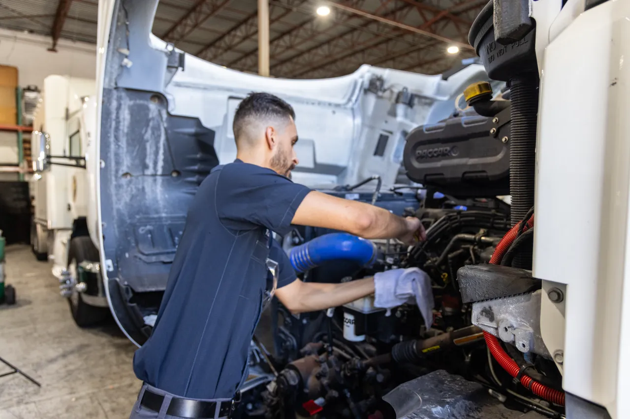 Preventive maintenance schedule service with technician inspecting commercial truck engine in repair shop.