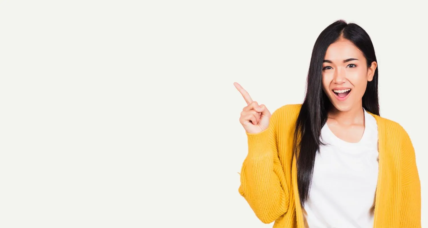 Smiling woman in a yellow cardigan pointing to blank space beside her