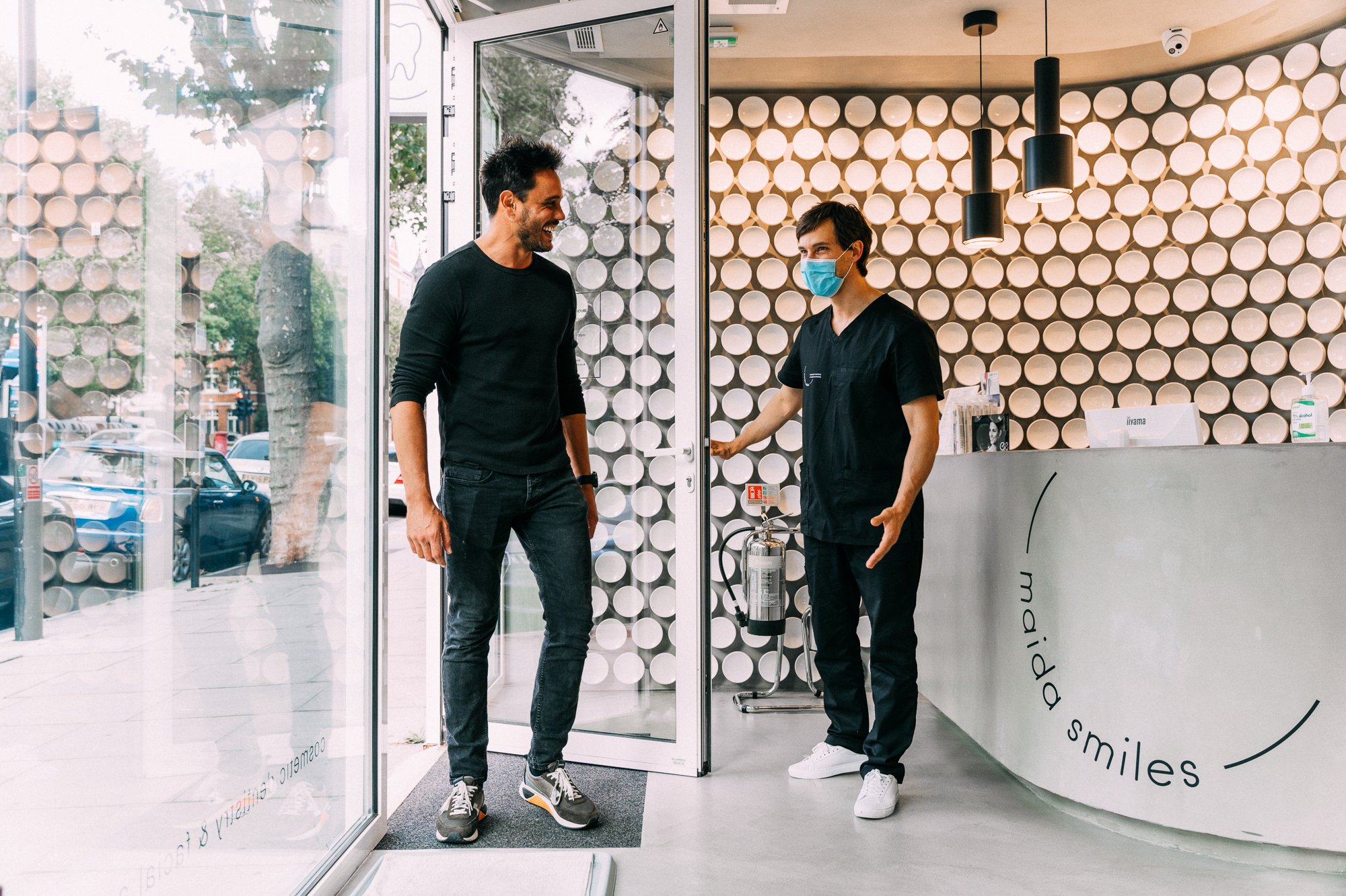 Clinician gesturing to welcome a patient into the reception area of the dental practice