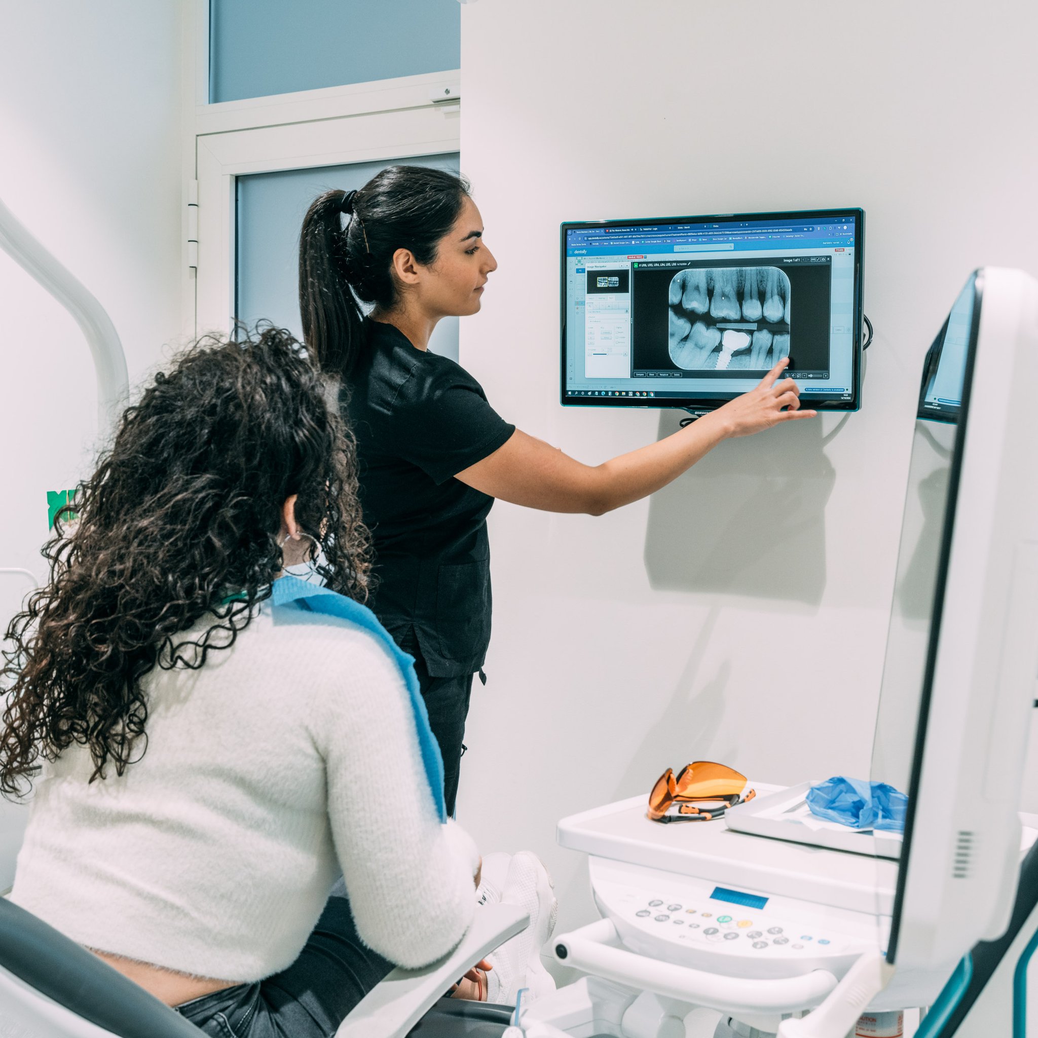 Dentist pointing to a dental implant x-ray on a wall monitor