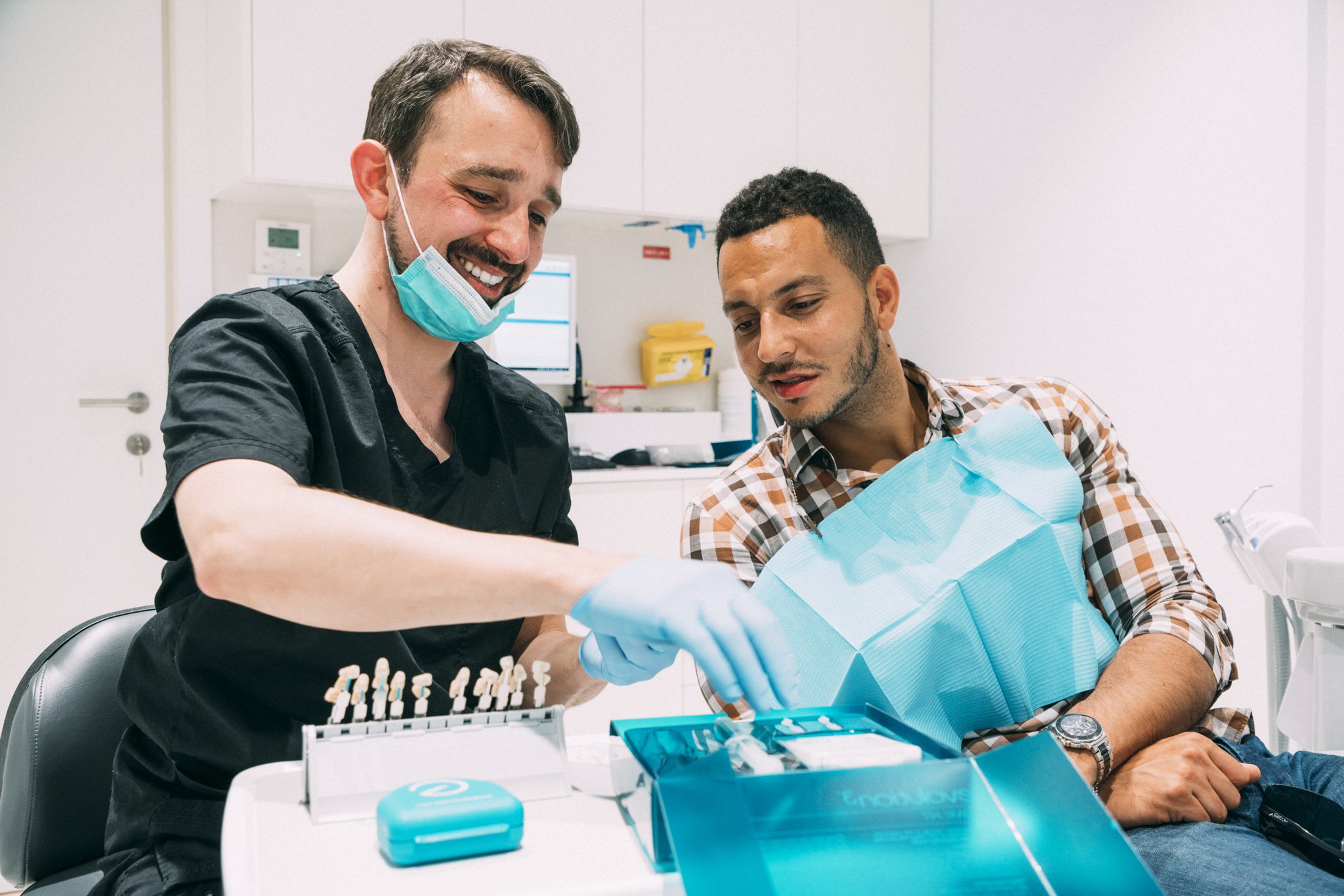 Dentist and patient smiling together while looking at tooth shade samples in a treatment room
