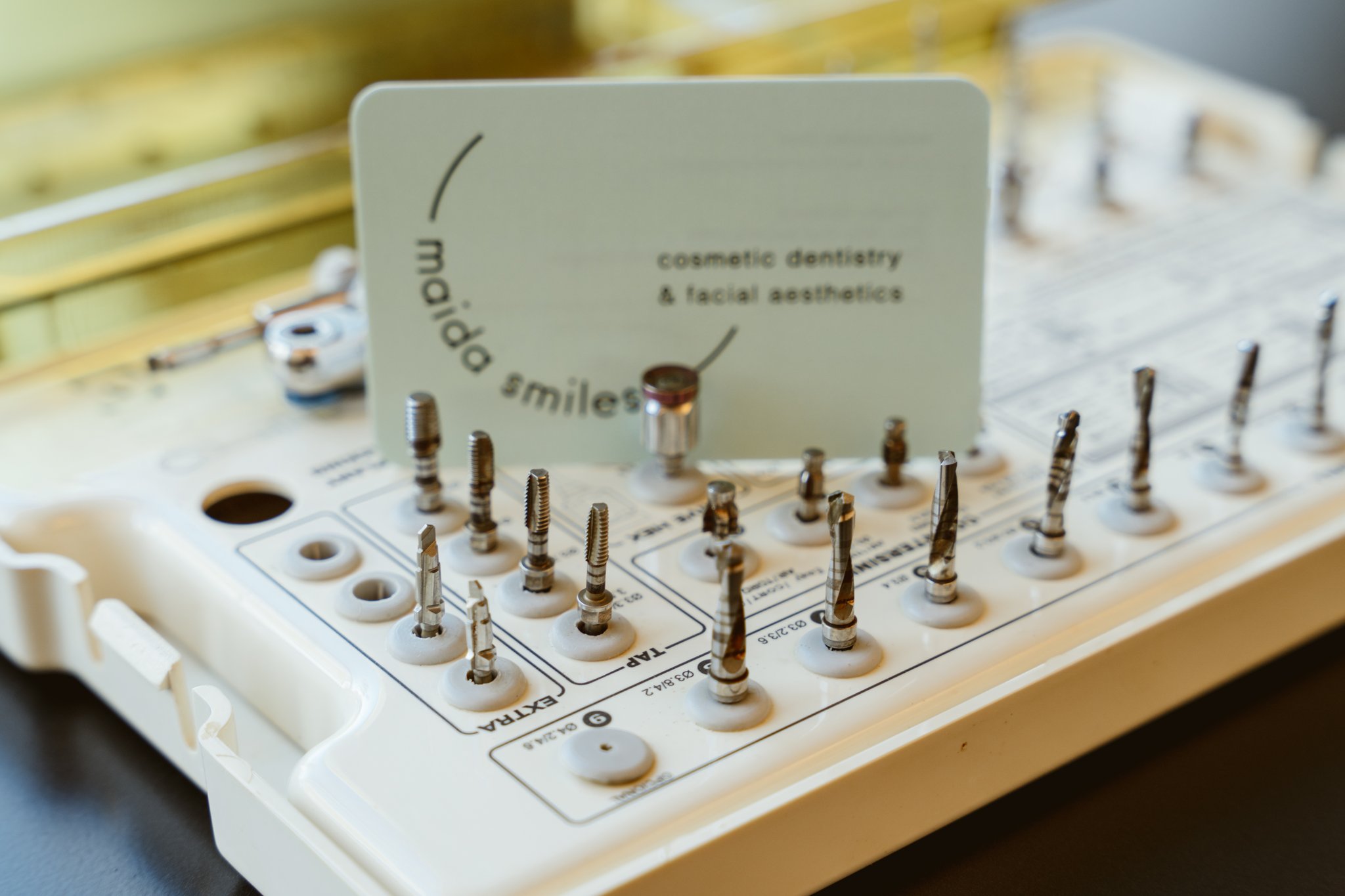 Implant surgical kit tray next to gold sterilisation box with Maida Smiles card