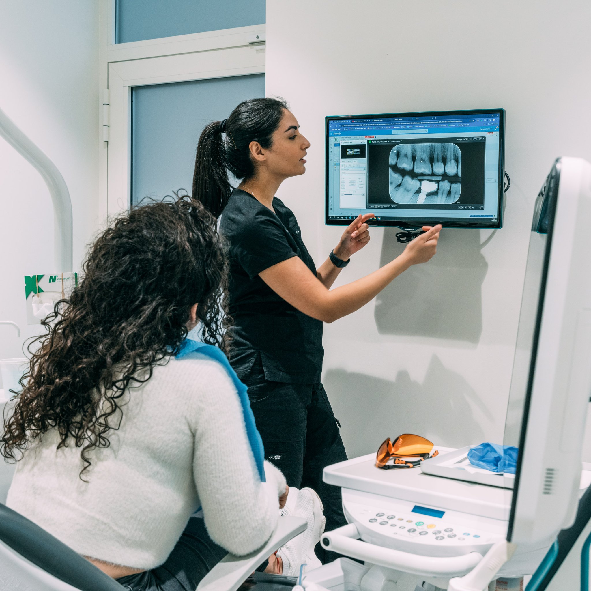 Side view of dentist pointing at an implant x-ray on a monitor