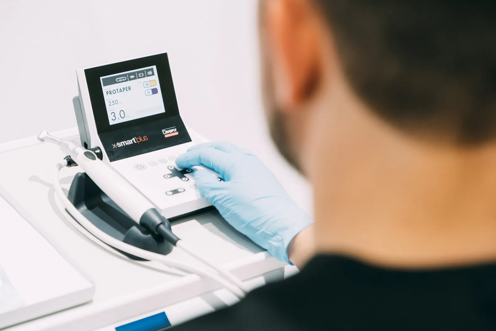 Gloved hand holding an electronic endodontic handpiece beside its control unit