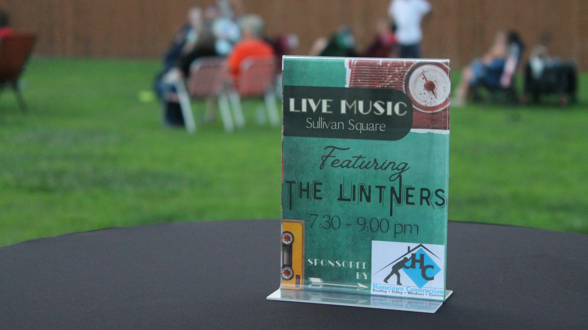 Table sign advertising live music at Sullivan Square featuring The Linters from 7:30 to 9:00 pm, sponsored by Hometown Construction.