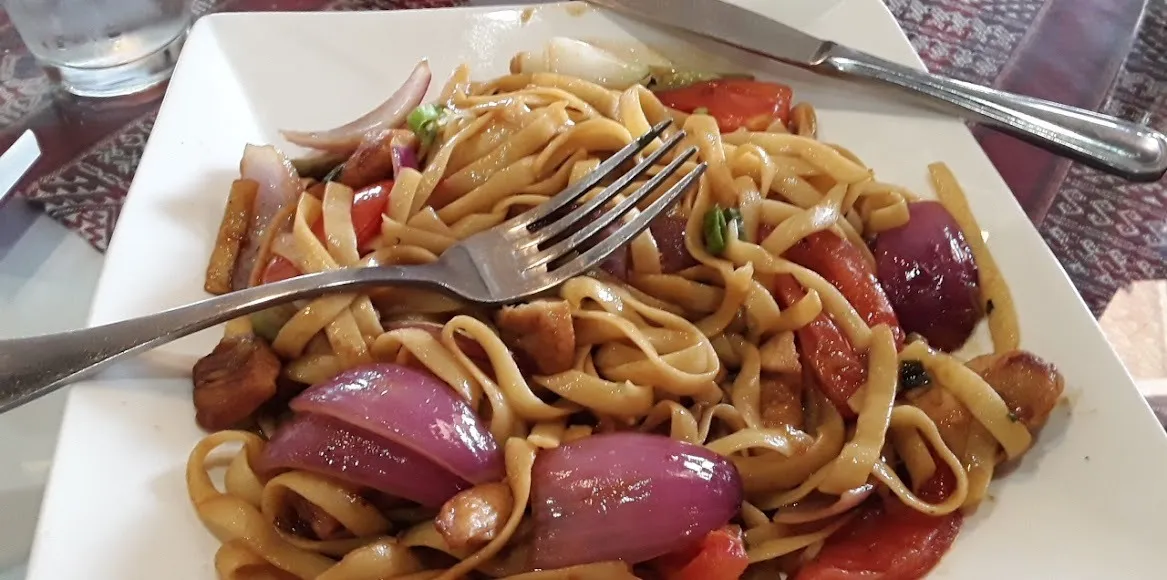 A plate of colorful noodles topped with mixed vegetables, accompanied by a fork resting beside it.
