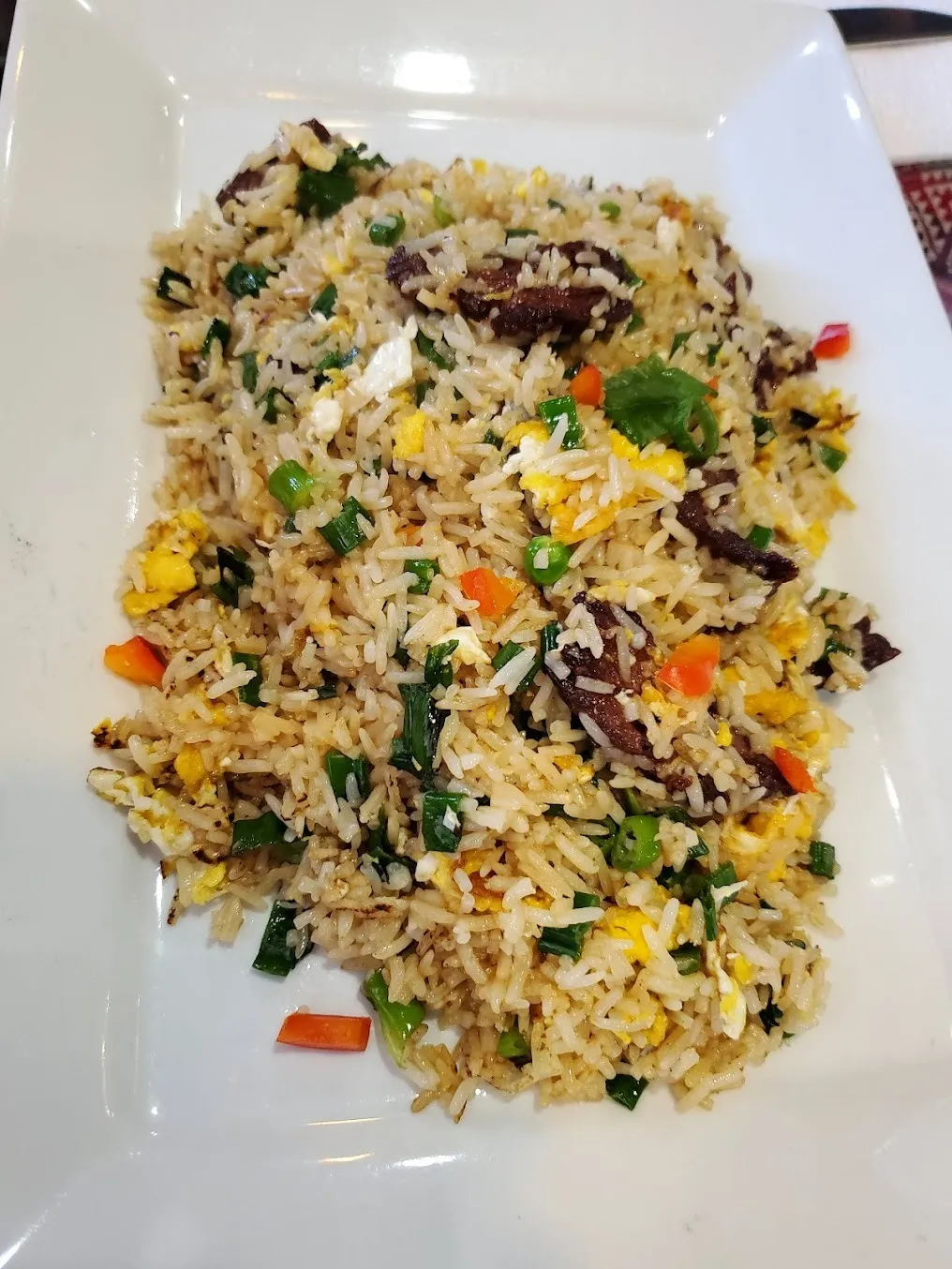 A plate of fried rice topped with assorted meats and colorful vegetables, garnished for presentation.