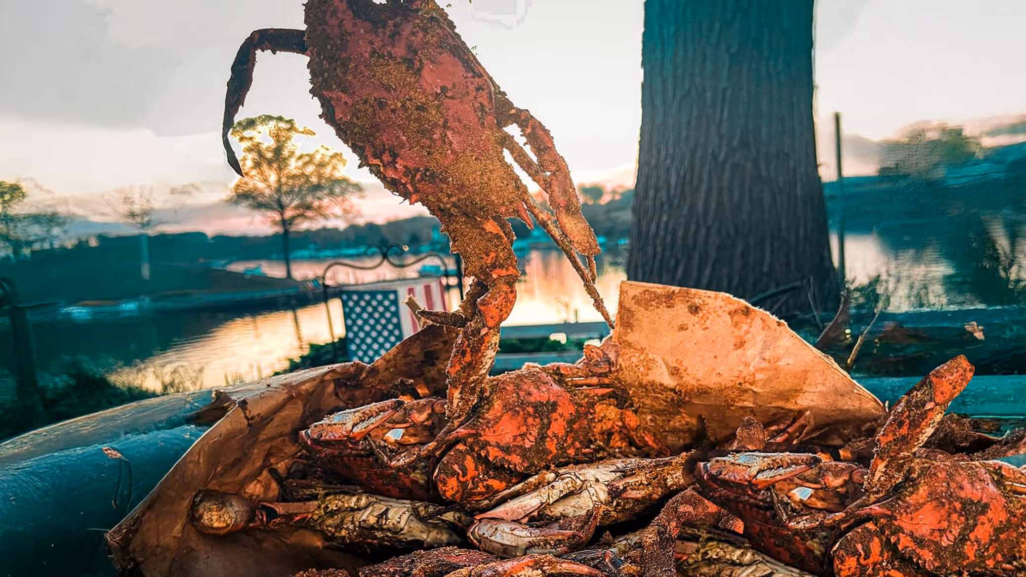Steamed crab covered in seasoning held above a paper-covered table with more crabs.