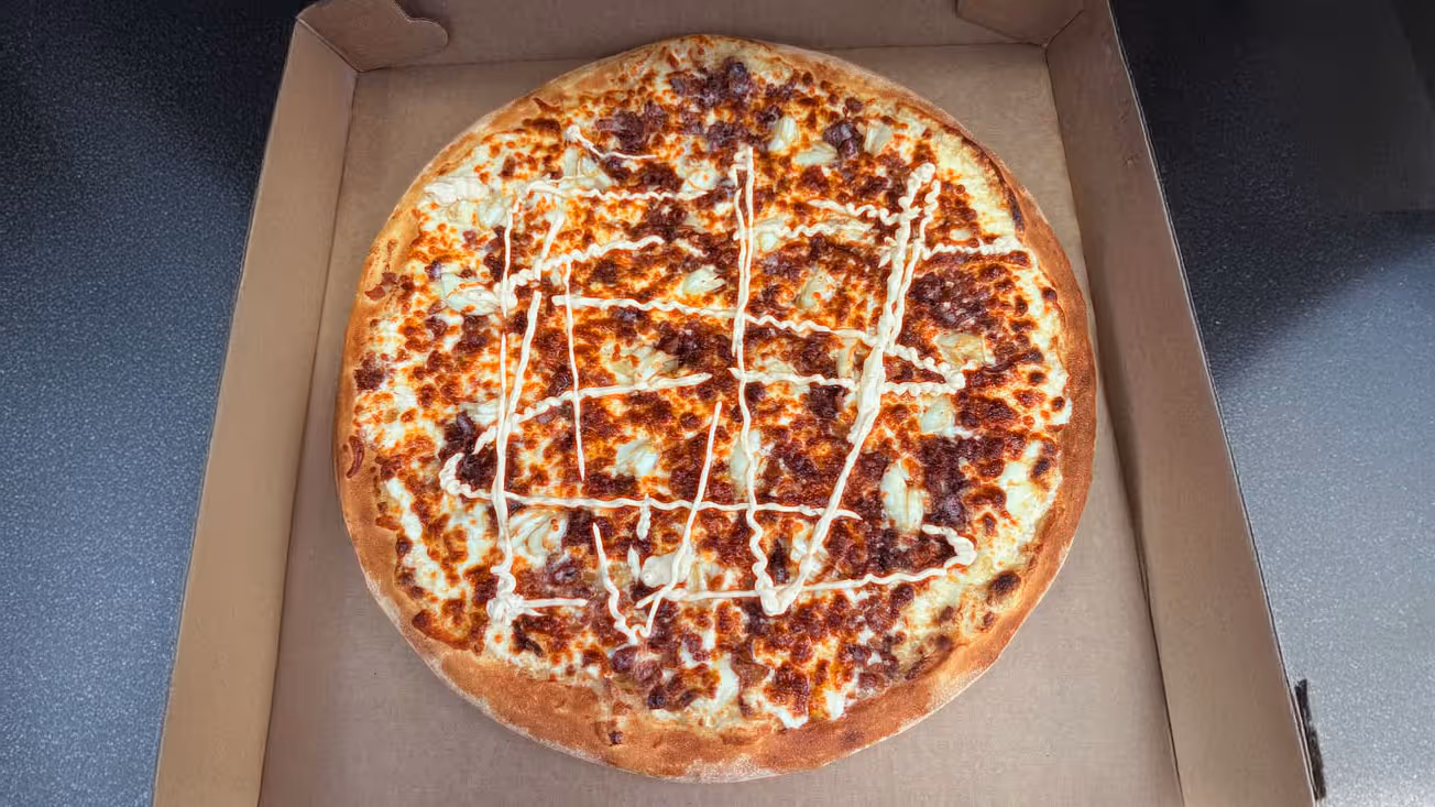 Pizza in an open box, topped with melted cheese.