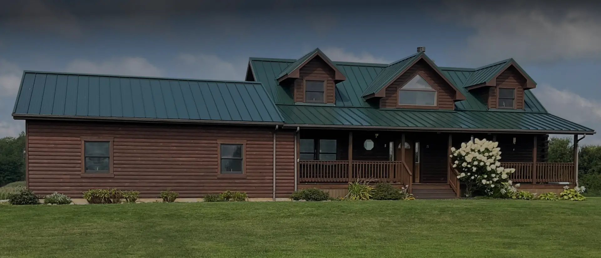 Rustic log cabin-style home with green standing seam metal roofing, installed by Twincreek Roofing in rural Ohio.