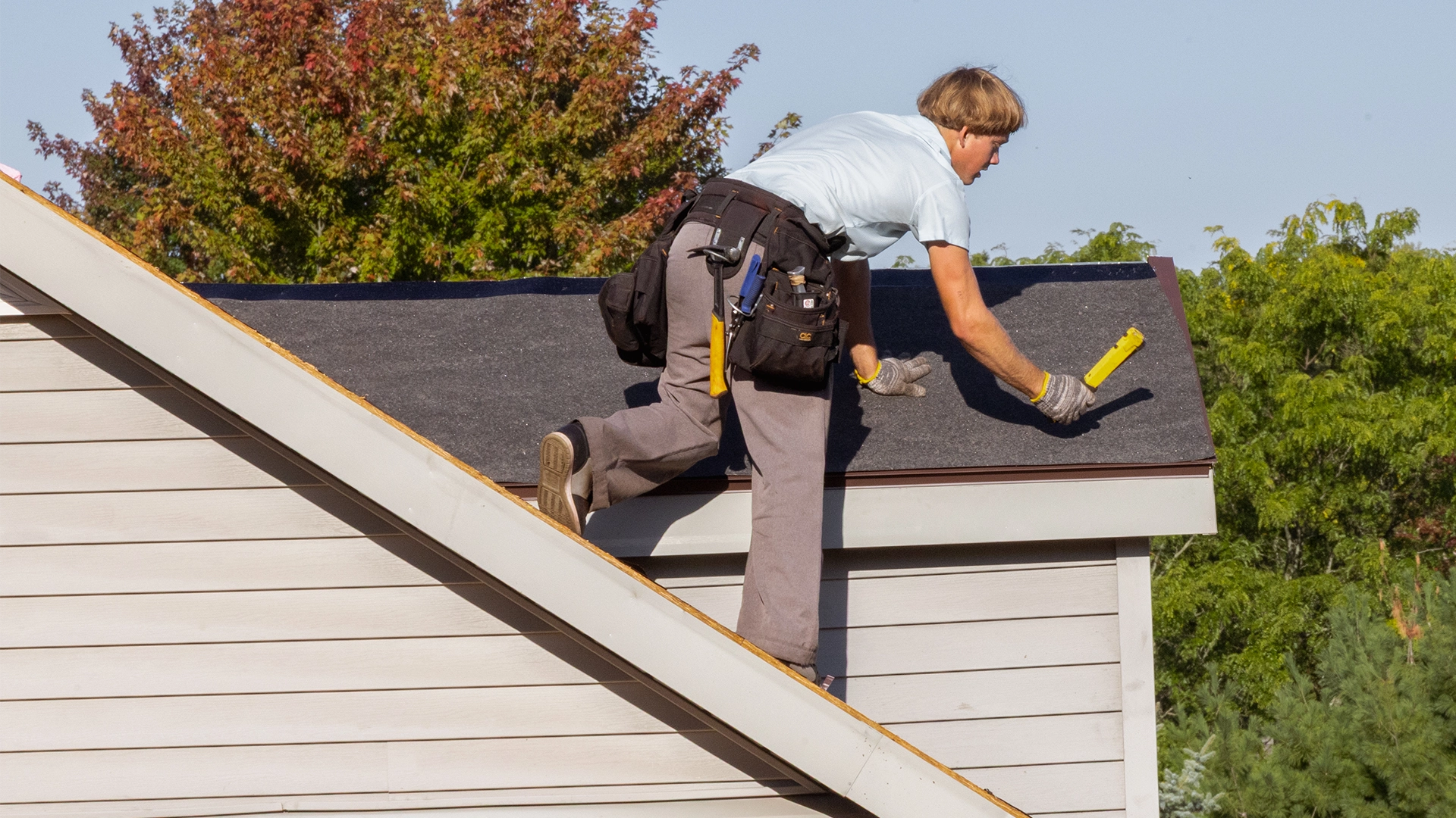Construction worker on top of a shingled roof with tan siding