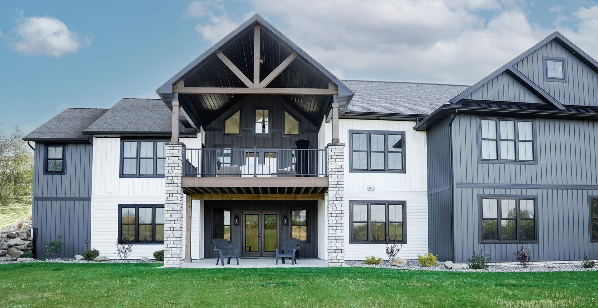 Home with back porch and patio with white and dark grey siding and with brick pillars